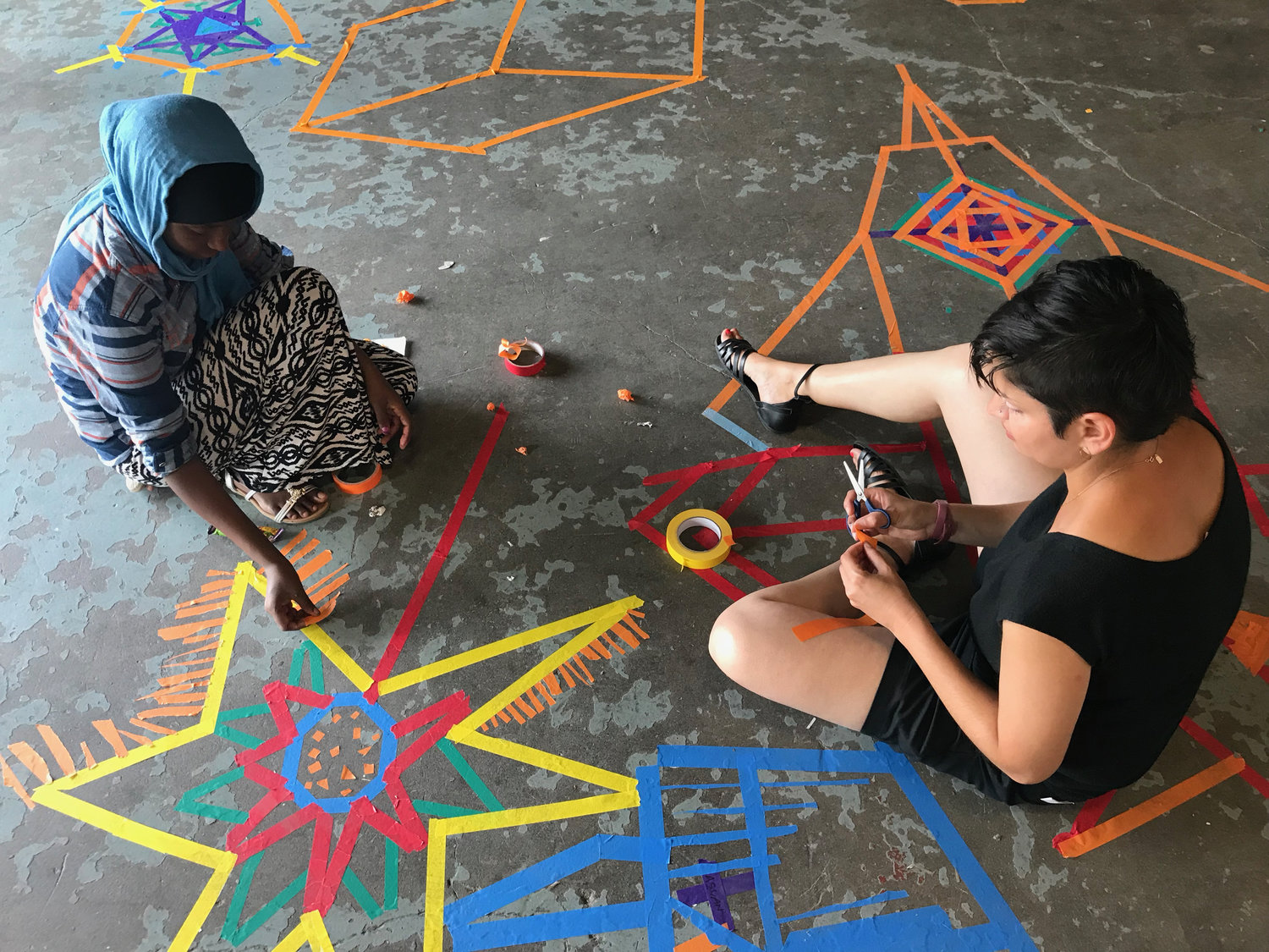 Two students sitting on the ground making designs using pieces of colored tape